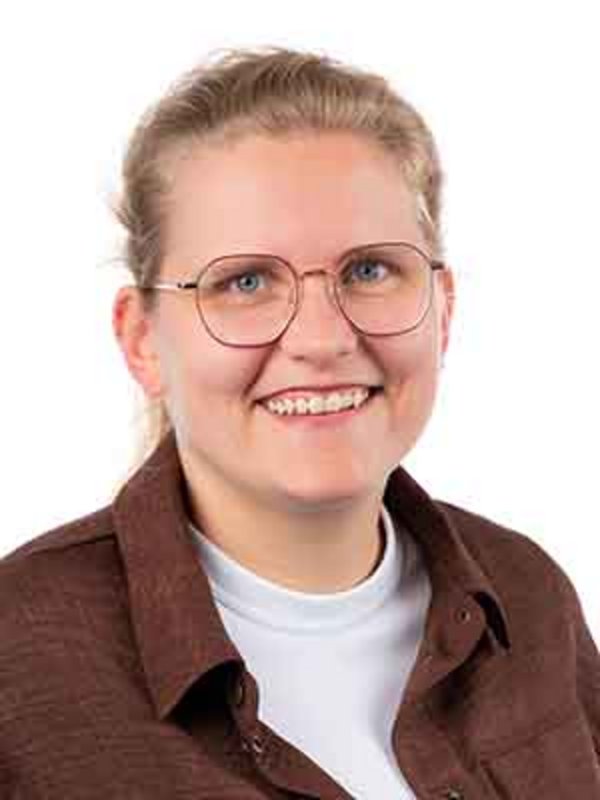 UKM Pädiatrische Hämatologie und Onkologie | Amelie Alfert | Trägt eine Brille, ein weißes T-Shirt und ein braunes Hemd drüber. Sie lächelt in die Kamera.