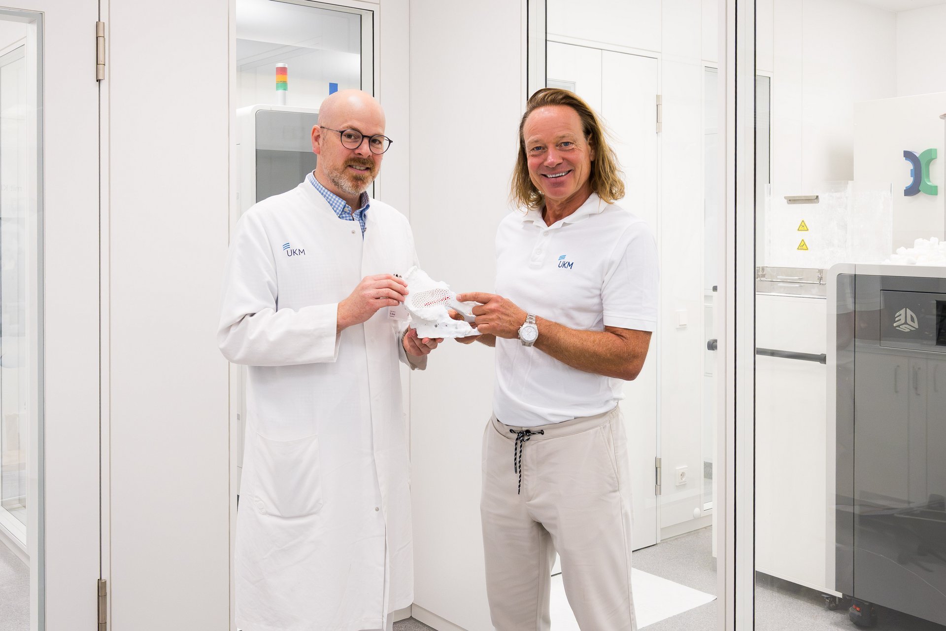 UKM | Die Klinikdirektoren der Unfallchirurgie und der Orthopädie halten ein anatomisches Modell in den Händen und lachen in die Kamera.