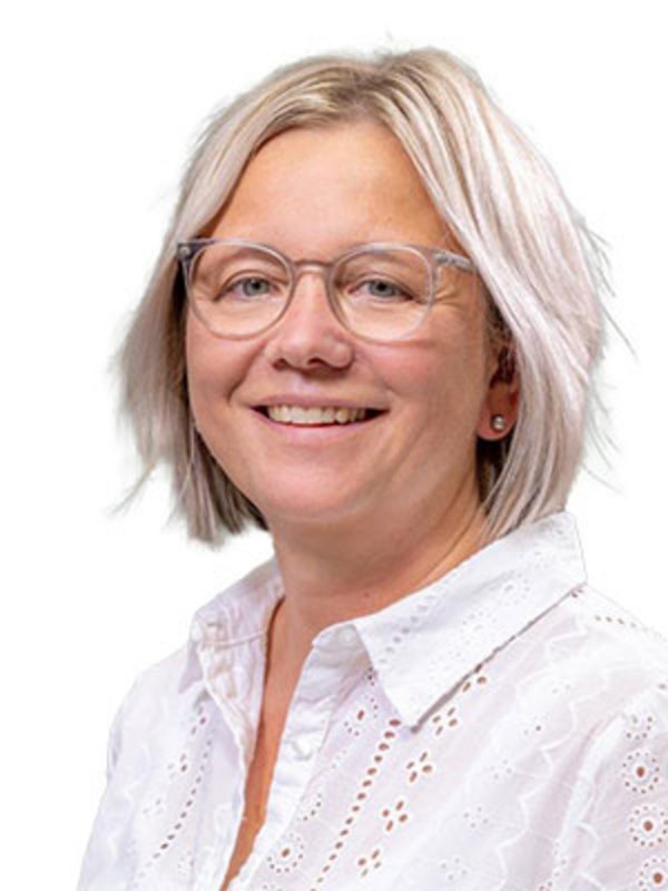 UKM Alterstraumazentrum | Portrait einer Mitarbeiterin. Sie trägt eine helle Brille und eine weiße Bluse, ist blond und lacht.