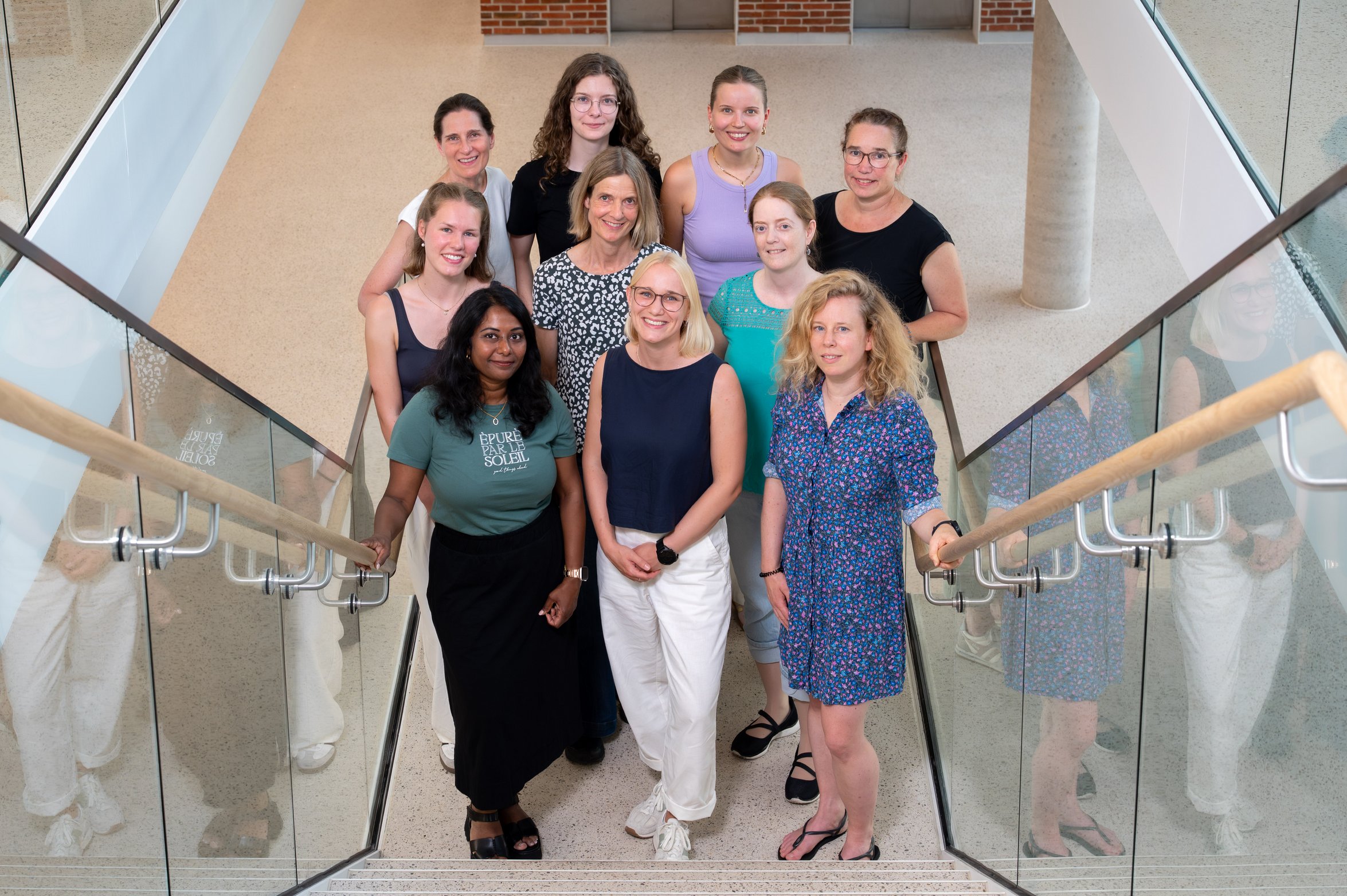 UKM Pädiatrische Hämatologie und Onkologie | Gruppenbild der AG Rössig, 10 Frauen stehen am unteren Rand einer Treppe und schauen leicht hoch in die Kamera