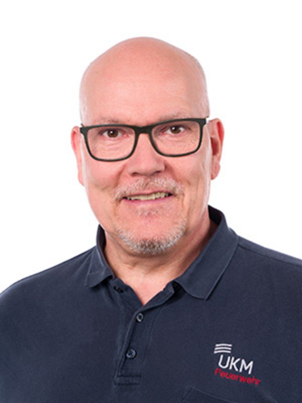 UKM Werkfeuerwehr | Jörg Lehmkuhl | Er trägt eine Brille und ein dunkelblaues Shirt und lächelt in die Kamera.