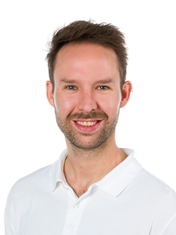 UKM | Portrait von Julian Hasselmann aus der Orthopädie. Er trägt ein weißes Hemd und lächelt.