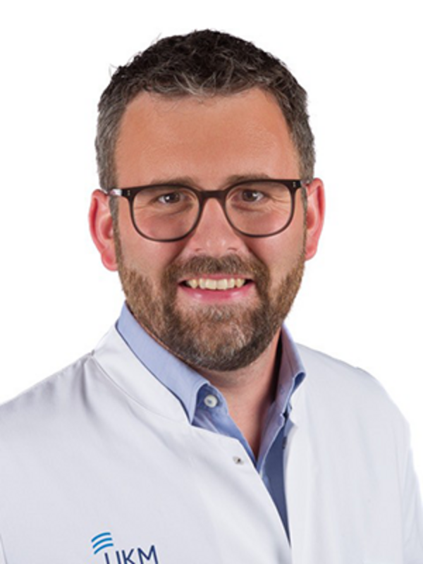 UKM | Portrait eines Arztes der Unfallchirurgie. Er trägt einen weißen Kittel und lächelt.