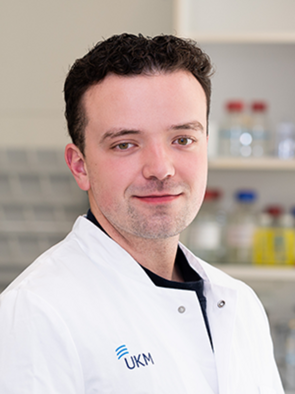 UKM | Portrait eines Mitarbeiters im Forschungsteam der Klinik für Endovaskuläre und Vaskuläre Chirurgie | Er trägt einen weißen Kittel und lächelt