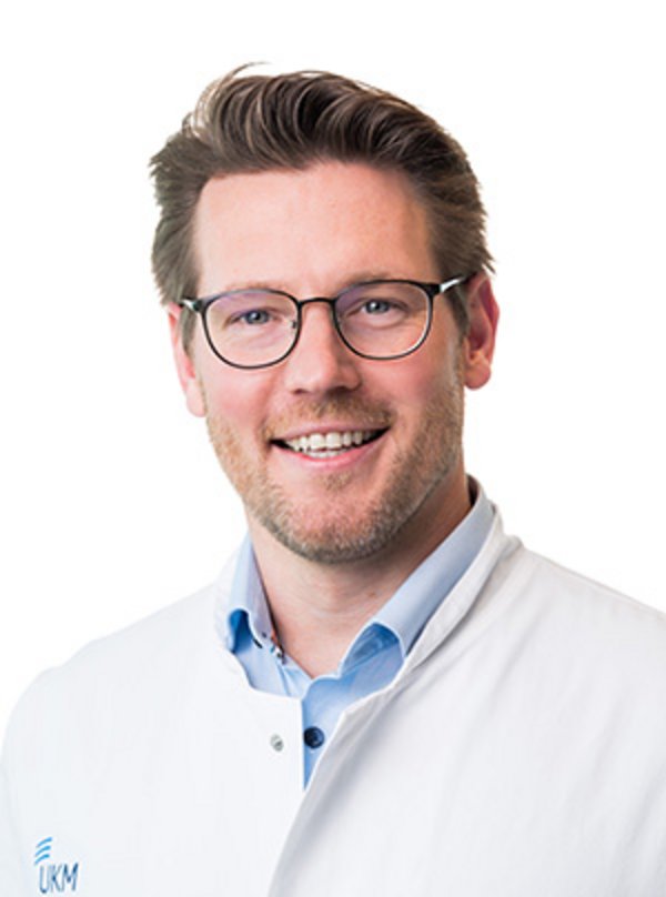 UKM Plastische Chirurgie | Nils Otto | Mann mit braunen Haaren und Brille lächelt in die Kamera.