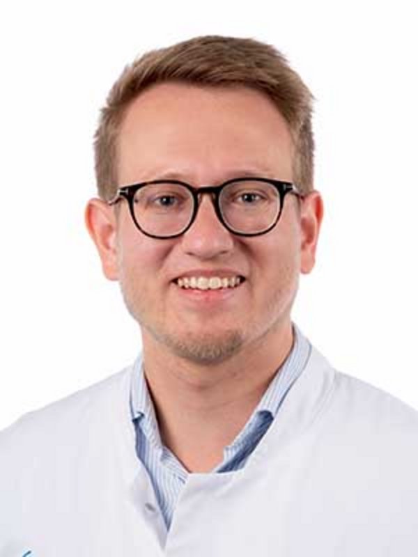 UKM Klinik für Psychosomatische Medizin und Psychotherapie | Stefan Kahnert | Trägt einen Kittel und eine Brille und lächelt in die Kamera.