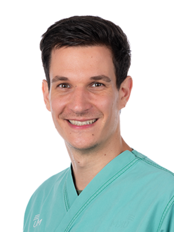 UKM | Portraitaufnahme von Arzt aus der Medizinischen Klinik B. Er trägt einen türkisfarbenen Kasack und lacht.