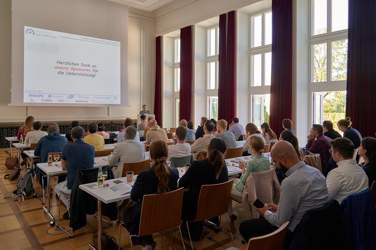 UKM Herz-MRT-Zentrum | Saal mit Leuten, Präsentation an der Wand.