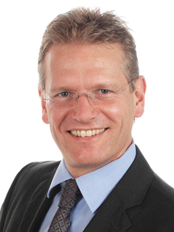 UKM | Portrait von Neuroradiologe Wolfram Schwindt. Er trägt dunklen Sakko und Krawatte und lacht.