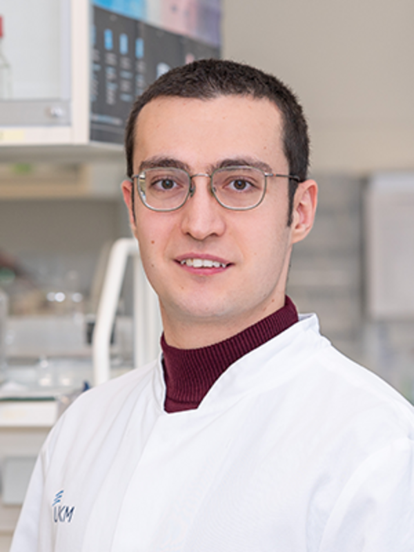 UKM | Portraitaufnahme eines Mitarbeiters im Forschungsteam der Klinik für Endovaskuläre und Vaskuläre Chirurgie | Er trägt einen weißen Kittel und lächelt