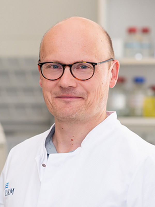 UKM | Portraitaufnahme des Laborleiters Vasuläre Biologie der Klinik für Endovaskuläre und Vaskuläre Chirurgie | Er trägt eine Brille, einen weißen Kittel und lächelt