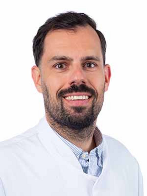 UKM Radiologie | Philip Schindler | Lächelt in die Kamera und trägt einen weißen Kittel..