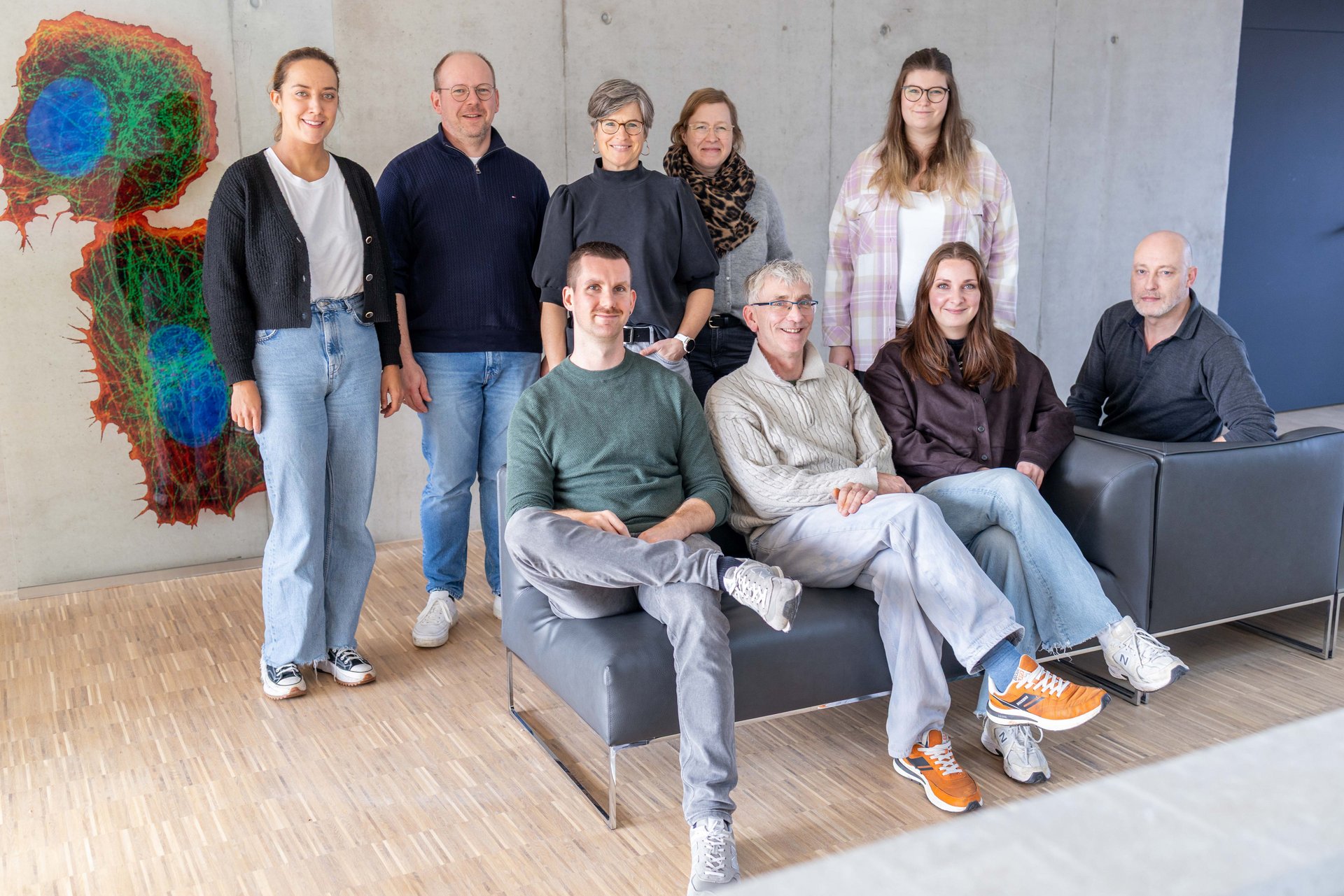 UKM Magnet | Gruppenbild von fünf Frauen und vier Männern. Vier Frauen und ein Mann stehen hinter einem Sofa. Die anderen drei Männer und eine Frau sitzen auf diesem. 