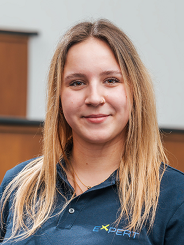 UKM | Portrait einer Mitarbeiterin des Expert-Projekts. Sie trägt ein dunkelblaues Poloshirt und lächelt.