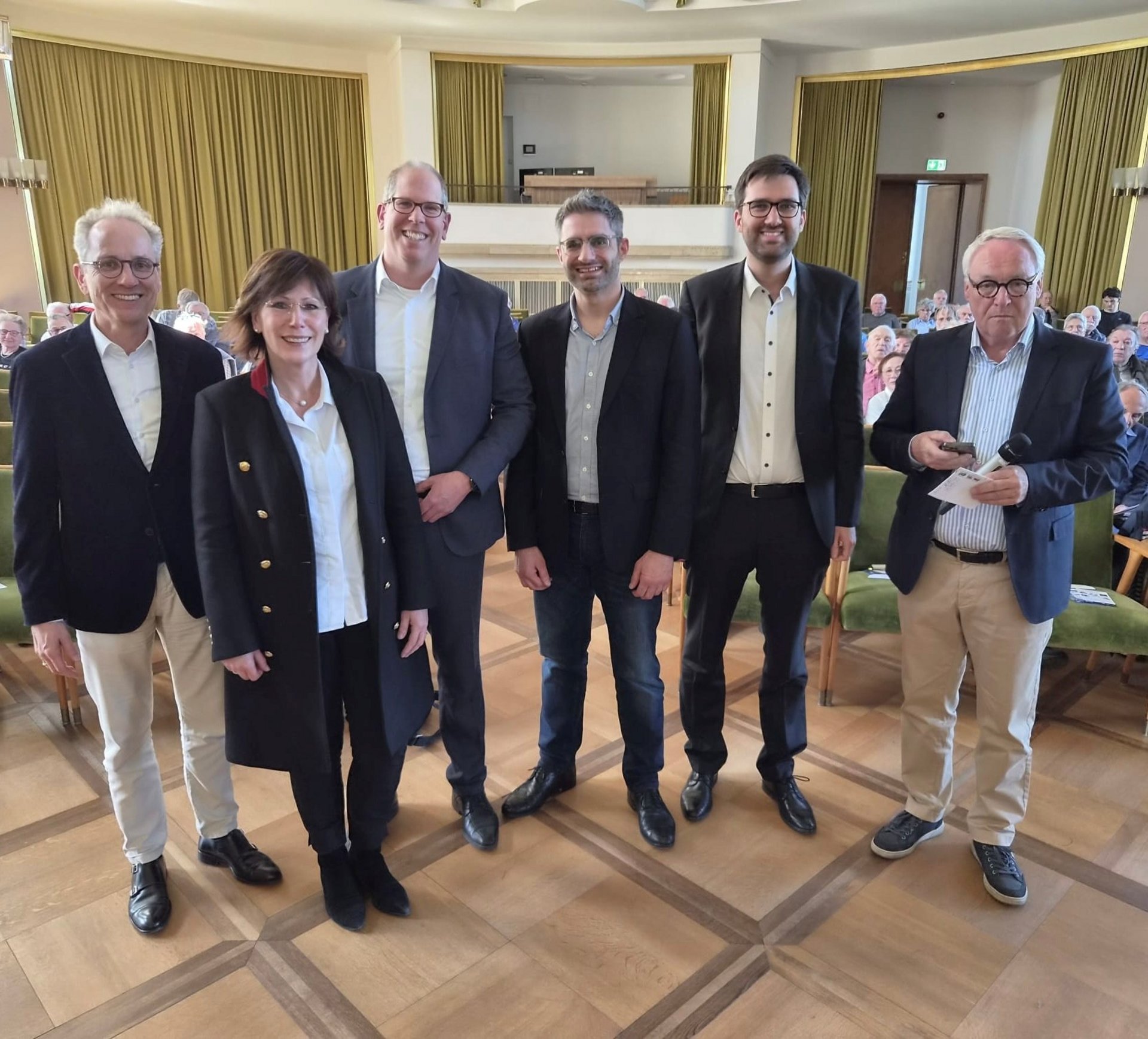 Gruppenbild in der Aula des Schlosses. Fünf Männer und eine Frau lächeln in die Kamera.