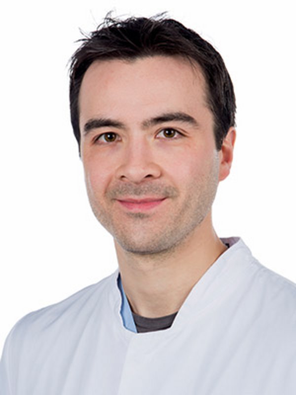UKM Medizinische Klinik D | Markus Döser | Er hat dunkle Haare, trägt einen weißen Kittel und lächelt in die Kamera.
