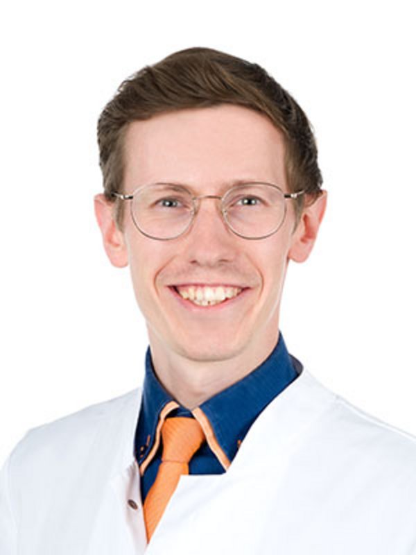 UKM Strahlentherapie | David Rene Steike | Er trägt einen weißen Kittel, eine Brille und lächelt in die Kamera.