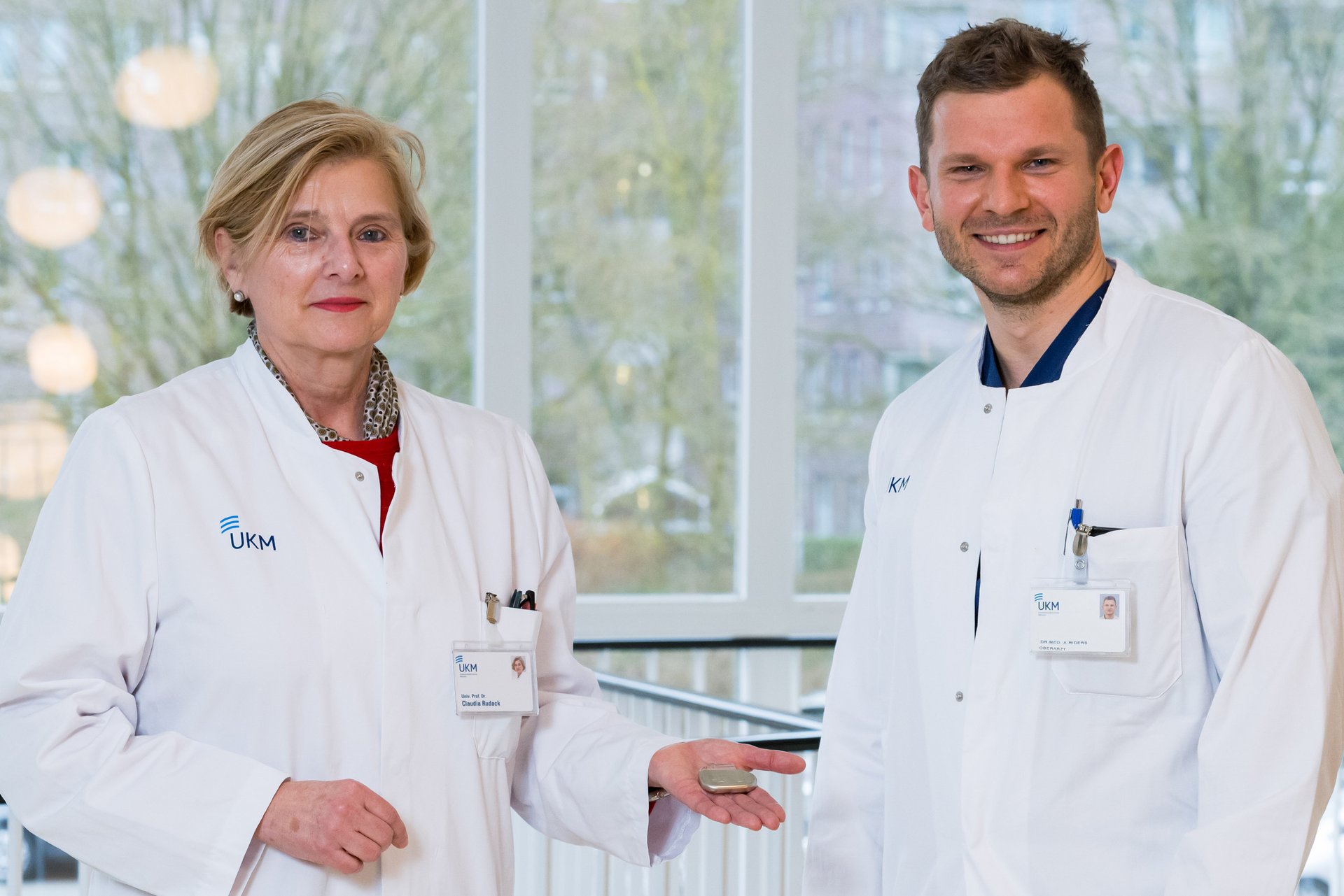 UKM | Eine Ärztin und ein Arzt aus der HNO-Klinik. Beide tragen weiße Kittel. Sie hält einen Zungenschrittmacher in der Hand.