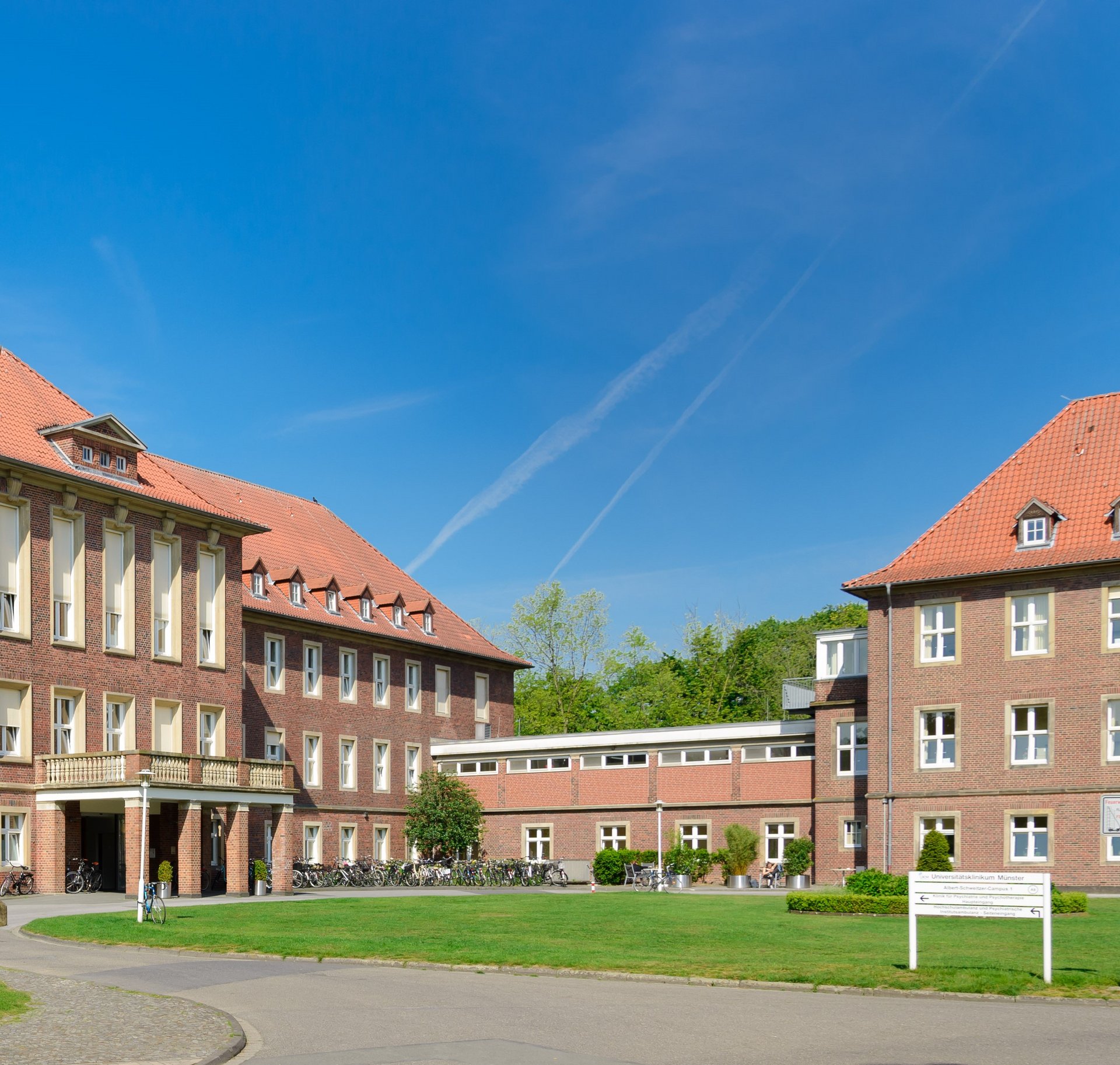 UKM PJ Broschüre | Bild des Gebäudes der Klinik für Psychische Gesundheit. Blauer Himmel, das Gebäude besteht aus roten Backsteinen. Im Vordergrund ist Rasen und ein weißes Schild zu sehen.