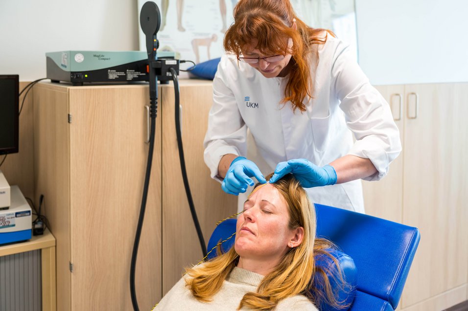 UKM | Presse | Patientin im blauen Behandlungsstuhl, eine Ärztin im weißen Kittel bringt Elektroden auf ihrem Kopf an