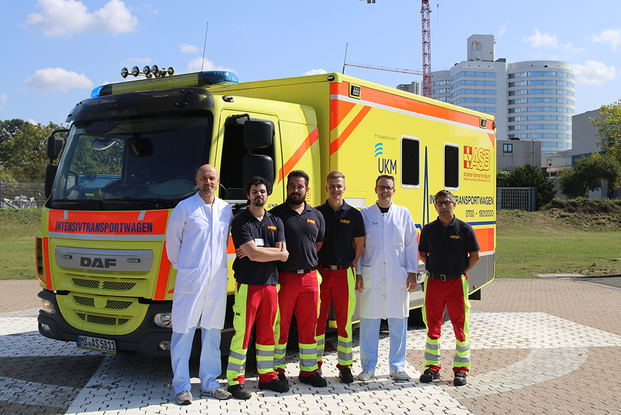 Zwei Ärzte aus der Internistischen Intensivmedizin und vier Notfallsanitäter vor einem Intensivtransportwagen des ASB Münsterland auf dem Hubschrauberlandeplatz des UKM