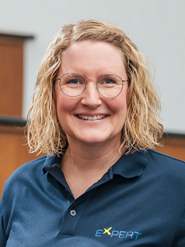 UKM | Portrait einer Mitarbeiterin des Expert-Projekts. Sie trägt ein dunkelblaues Poloshirt und lächelt