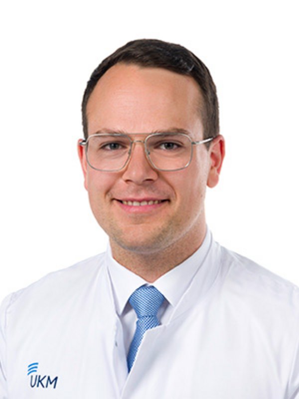 UKM Strahlentherapie | Marius Kreis | Er trägt einen weißen Kittel, eine Brille und lächelt in die Kamera.