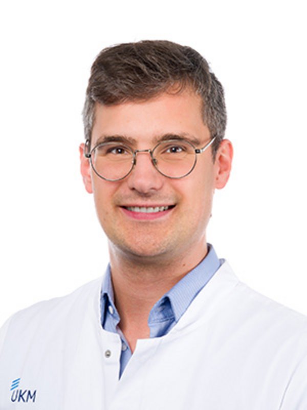 UKM Radiologie | Sebastian Kubasch | Trägt ein Brille und einen weißen Kittel und lächelt in die Kamera.