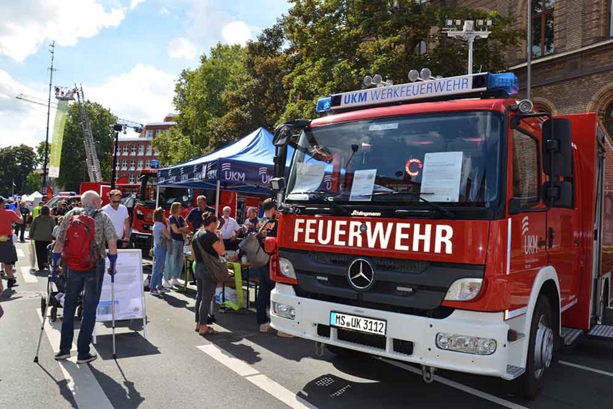 UKM Werkfeuerwehr | Ein Feuerwehrwagen ist von vorne zu sehen. Er steht auf einer Straße, neben diesem sind viele Menschen zu sehen.