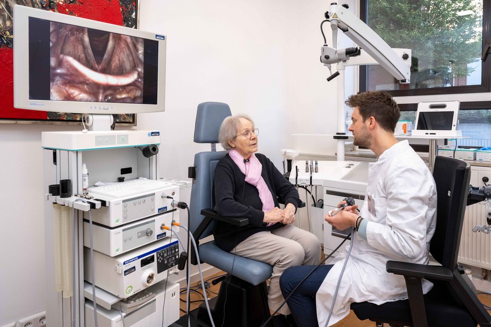 UKM | Behandlungszimmer mit Geräten und Monitor in der Phoniatrie. Patientin und Arzt sitzen sich gegenüber und sprechen miteinander.