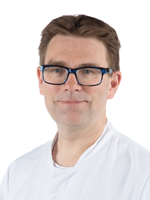 UKM | Portrait eines Arztes aus der Angiologie. Er trägt einen weißen Kittel und lächelt.