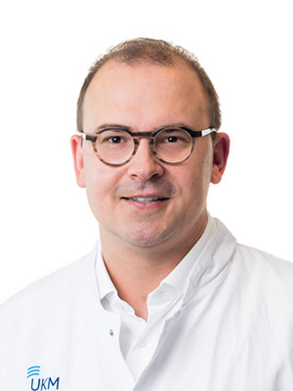 UKM Plastische Chirurgie | Nils Gebur | Mann mit Brille lächelt in die Kamera.