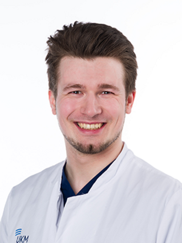 UKM | Arzt in der Unfallchirurgie. Er trägt einen weißen Kittel und lacht.