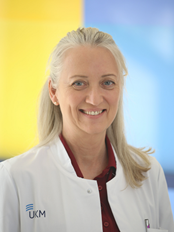 UKM | Portrait von Ärztin aus der Palliativmedizin. Sie trägt einen weißen Kittel und lächelt. Blau-gelber Hintergrund