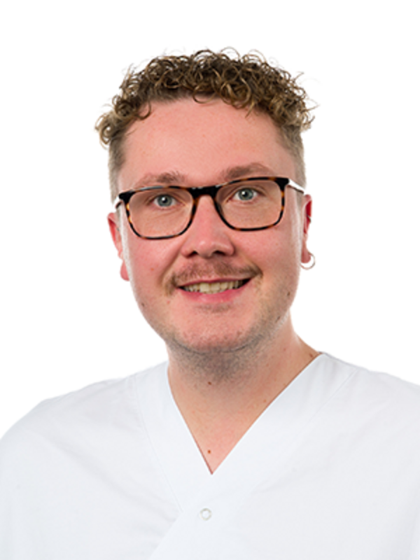 UKM Unfallchirurgie | Portrait von Pfleger Niklas Brüggemann. Er trägt Brille und einen weißen Kasack und lacht.
