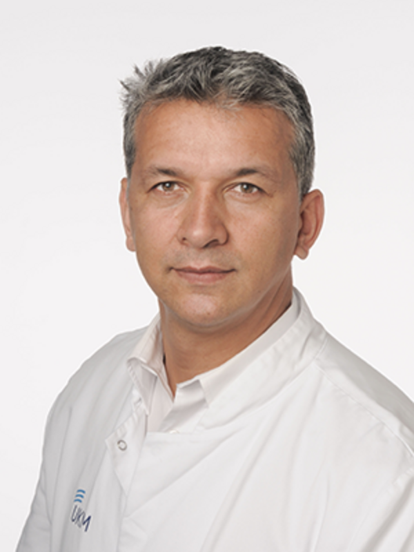 UKM | Portrait eines Arztes aus der Angiologie. Er trägt einen weißen Kittel und lächelt.