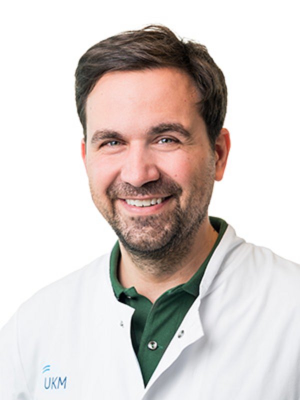 UKM Plastische Chirurgie | Johannes Zeller | Mann mit braunen Haaren und Bart lächelt in die Kamera.