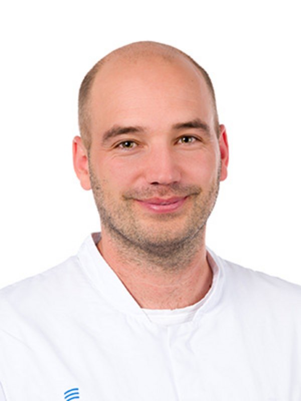 UKM Klinik für Neurologie | Michael Heming | Trägt einen weißen Kittel und lächelt in die Kamera.