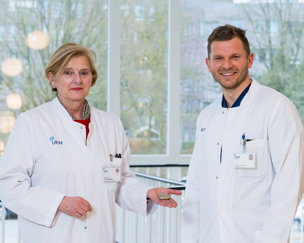 UKM | Eine Ärztin und ein Arzt aus der HNO-Klinik. Beide tragen weiße Kittel. Sie hält einen Zungenschrittmacher in der Hand.