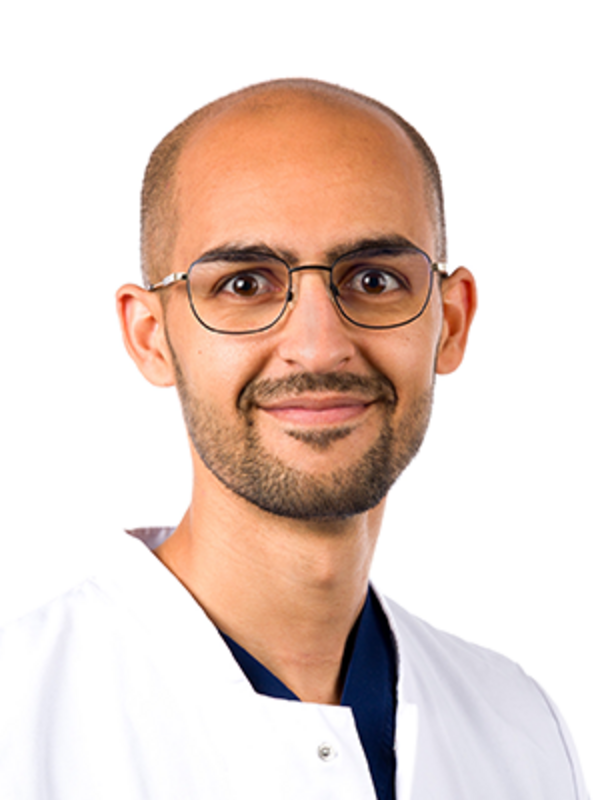 UKM Medizinische Klinik B | Portraitaufnahme von Ayoub Mortaji. Der Arzt trägt Brille, einen weißen Kittel und lächelt.