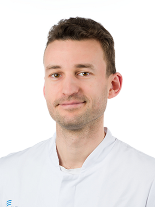 UKM | Zahnarzt der Klinik für Parodontologie. Er trägt einen weißen Kittel und lächelt.