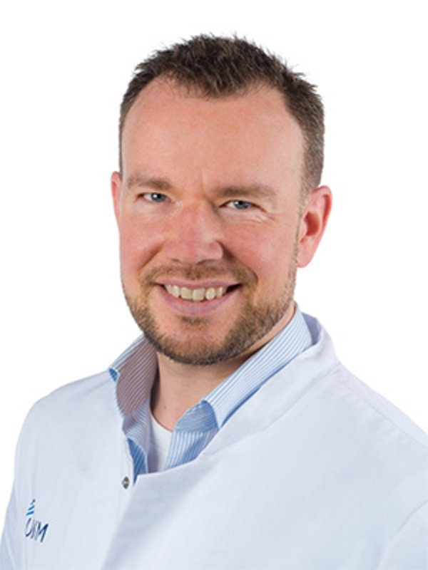 UKM | Portrait von Arzt aus dem Bereich Kardiologie. Er trägt einen weißen Kittel und lächelt.