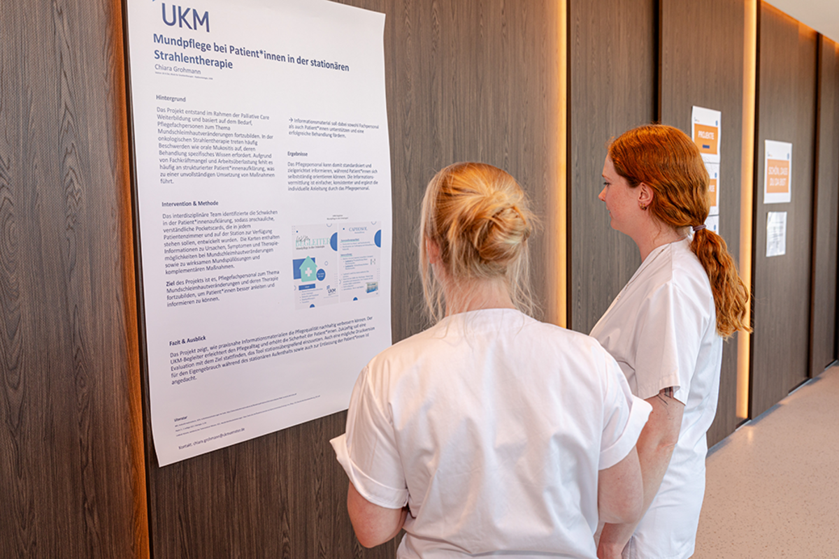 UKM | Zwei Pflegerinnen schauen auf ein Plakat zur Mundpflege bei Strahlenpatienten