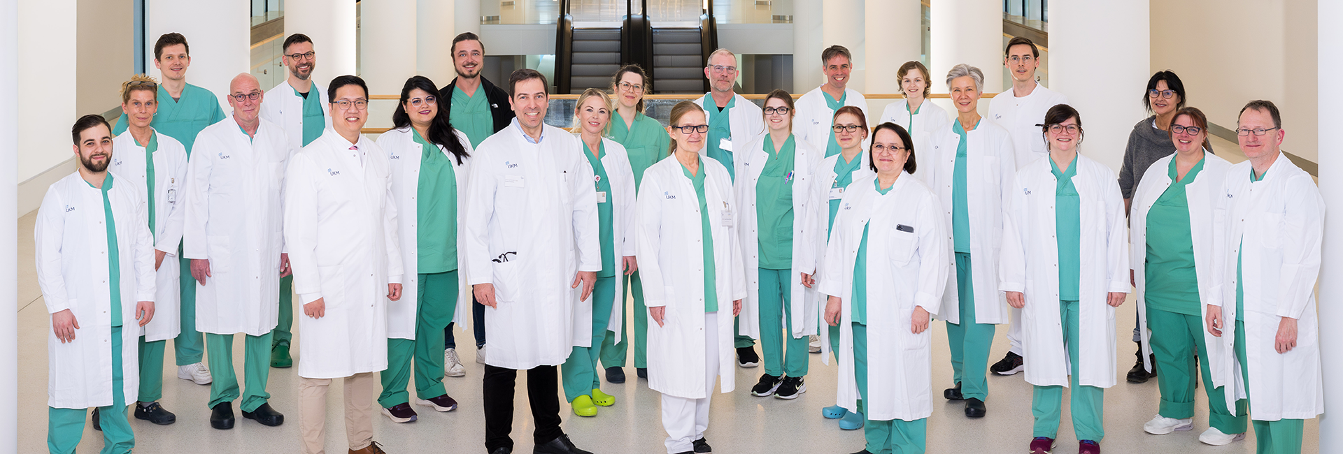 UKM | Gruppenfoto mit Teammitglieder der Endoskopie der Medizinischen Klinik B. Die Mitarbeitenden tragen weiße Kittel und grüne Kasacks und lachen.