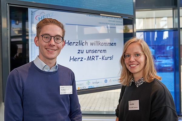 UKM Herz-MRT-Zentrum | Zwei Menschen vor dem Begrüßungsschild der Veranstaltung