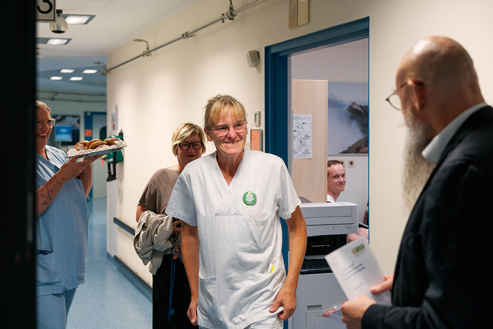 UKM Daisy Award | Andrea Kümpel kommt aus einem Zimmer auf der Station und wird von Mitarbeitenden mit dem Award überrascht.