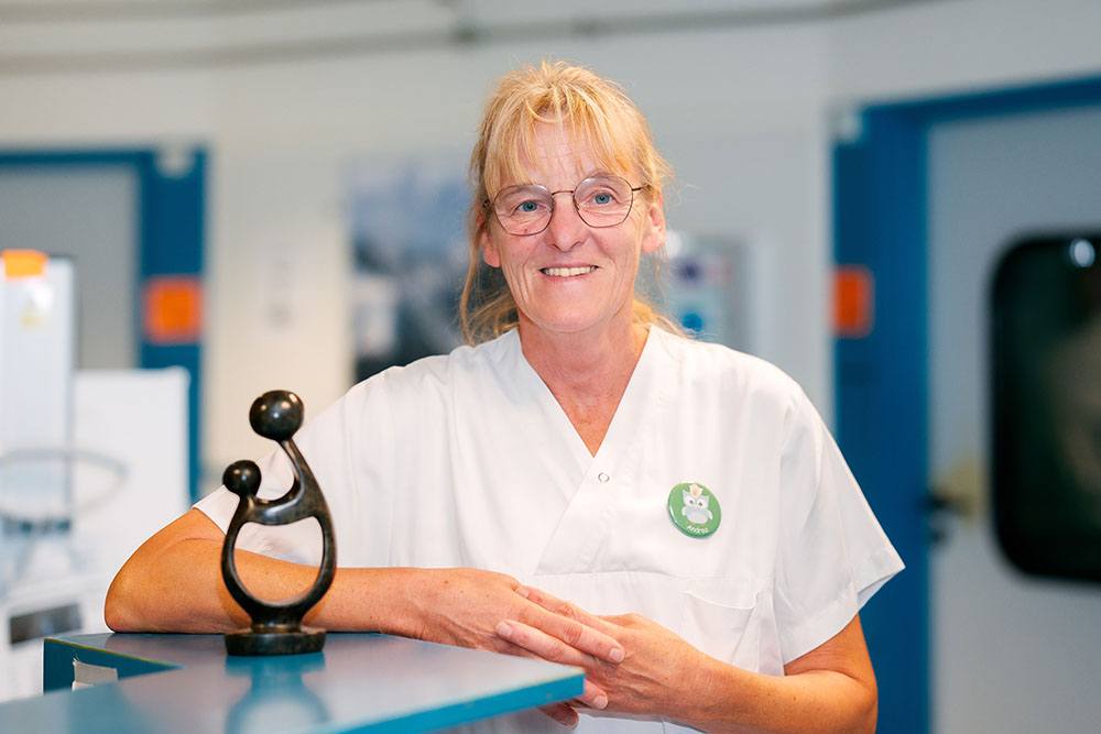 UKM Daisy Award | Andrea Krümpel lehnt am Stationscounter und lächelt in die Kamera. Neben ihr auf dem Tresen steht der Daisy Award.